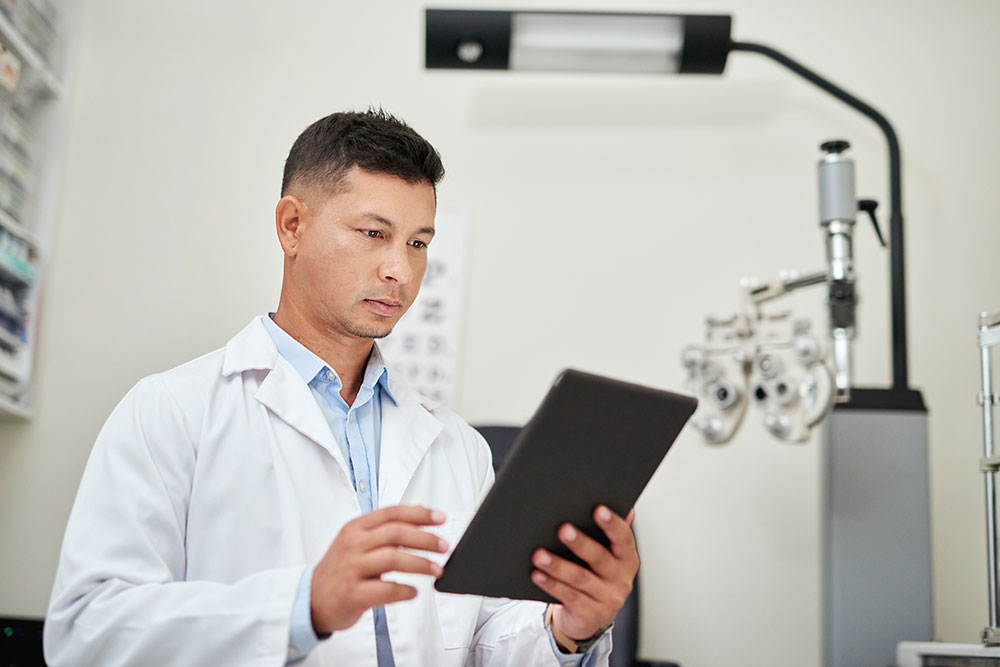 Tablet, optician and vision with a man optometrist doing research in his office for an eye exam or test. Healthcare, internet and optometry with a male eyecare professional at work for eyesight